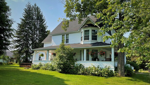 Une maison à deux étages avec un porche, entourée d’une pelouse bien entretenue et d’arbres.