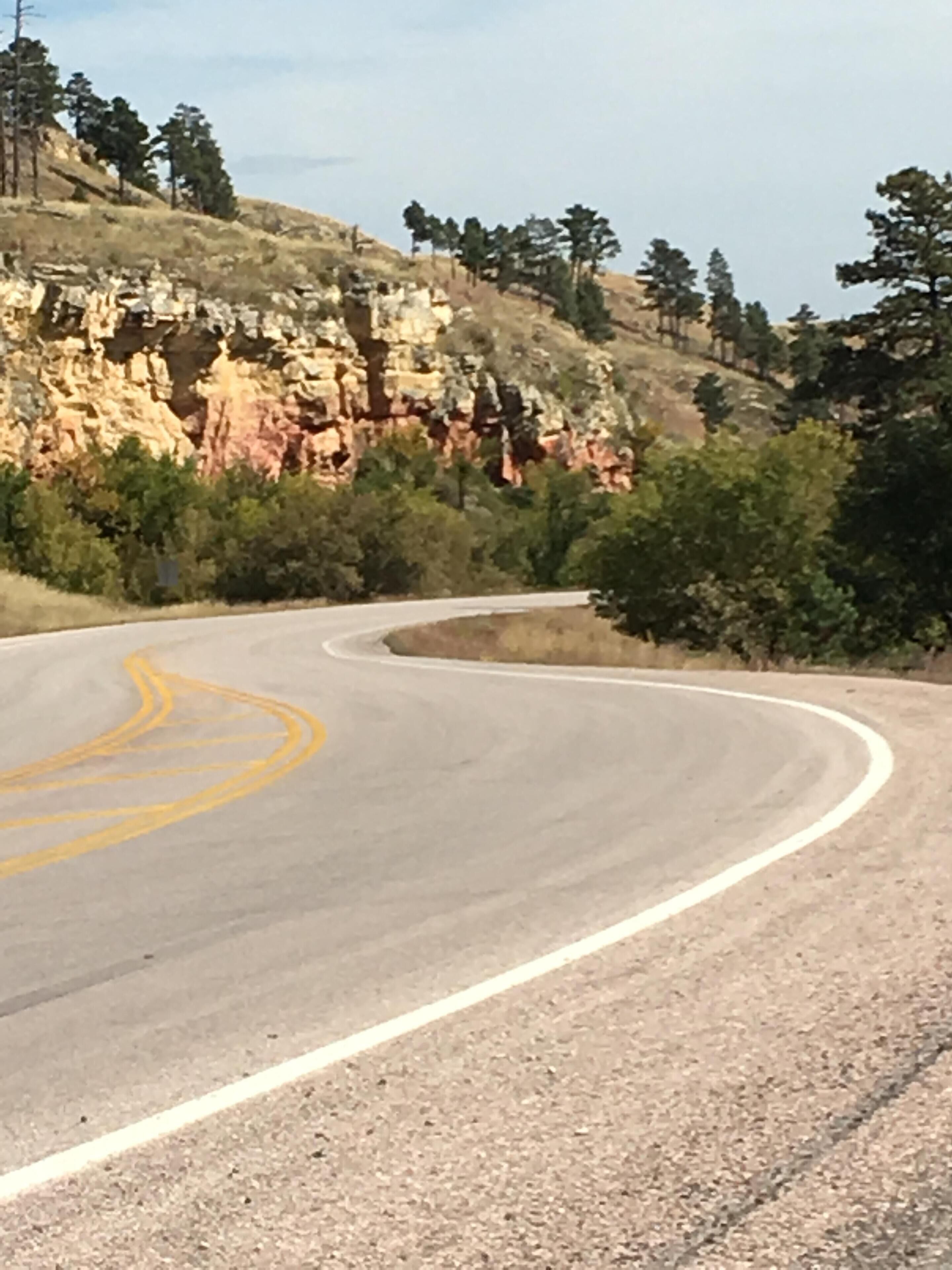 A winding road with yellow center lines, surrounded by rocky cliffs and sparse vegetation.