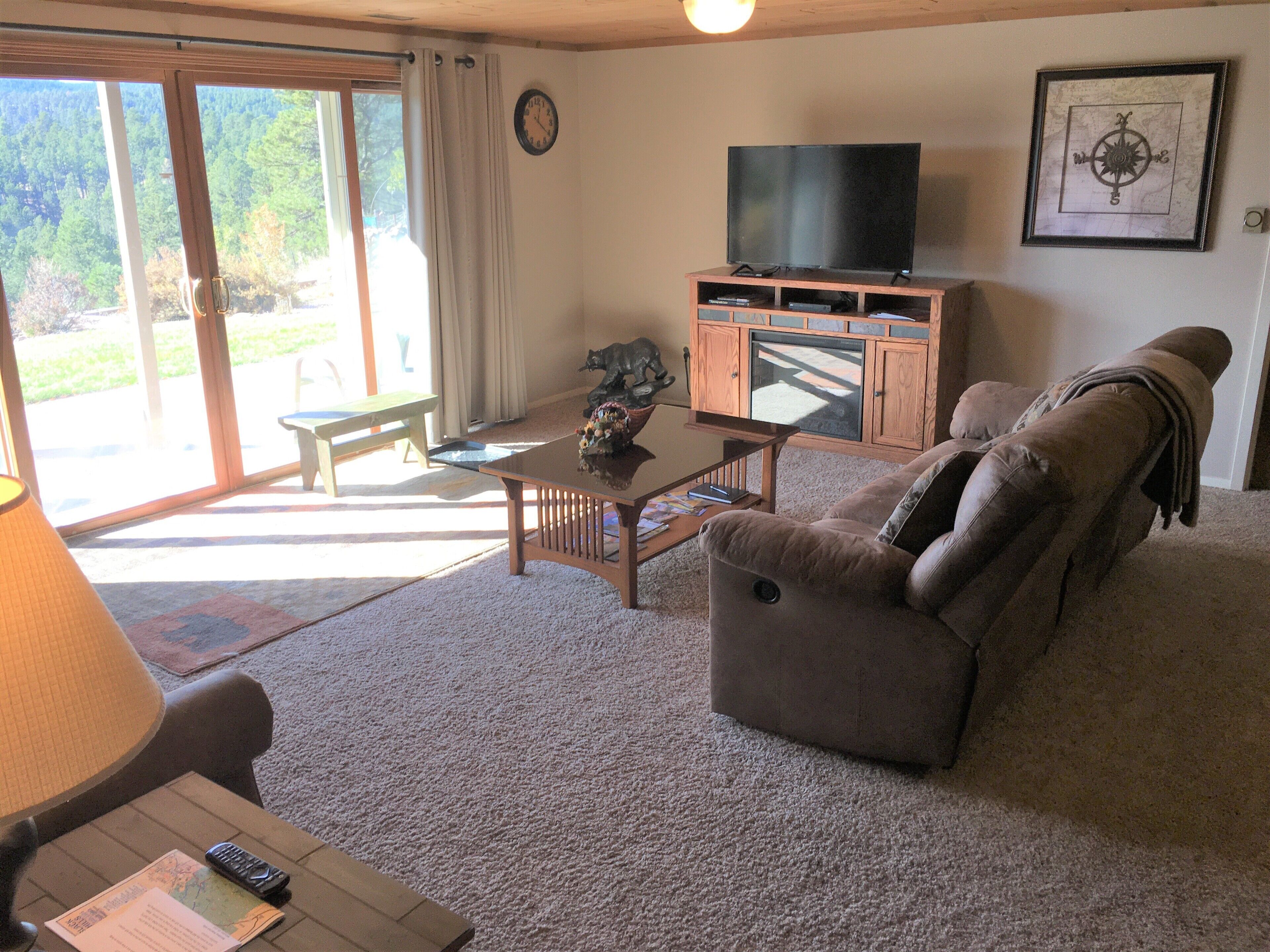 A living room with a sofa, a coffee table, a television on a wooden cabinet, and a window with curtains.