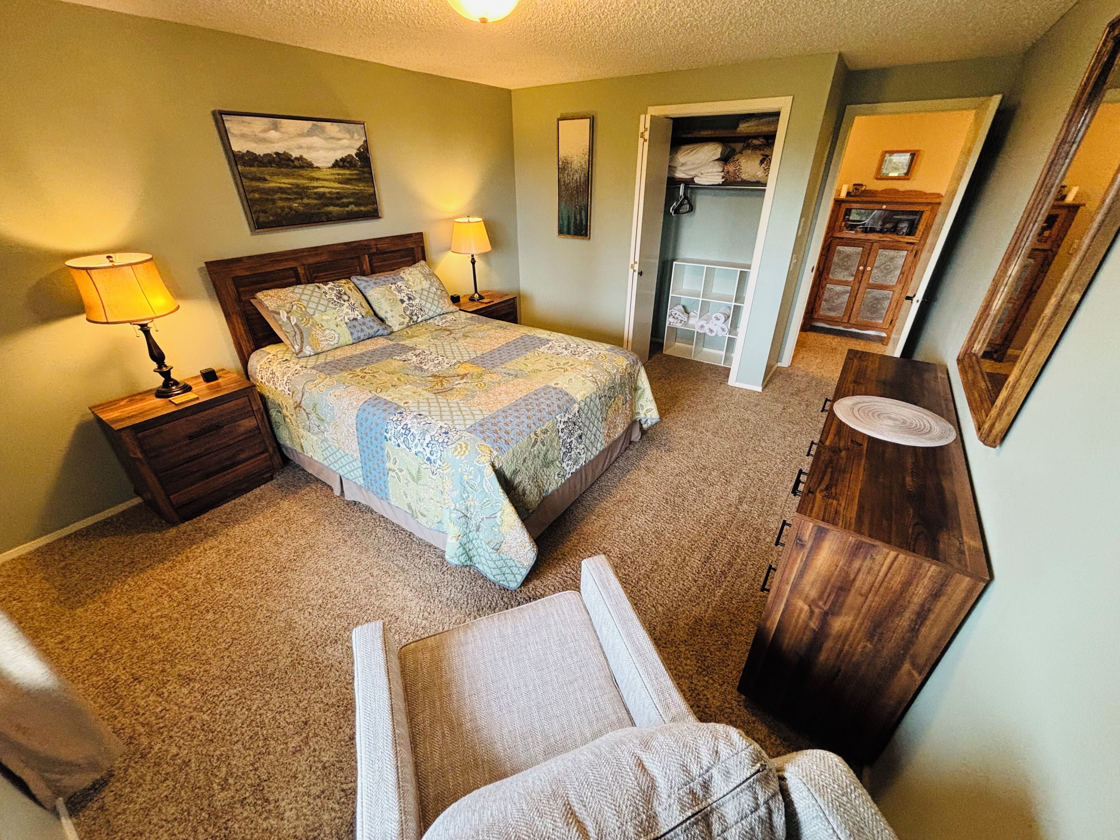A bedroom with a bed, nightstands, a dresser, a chair, and a closet.