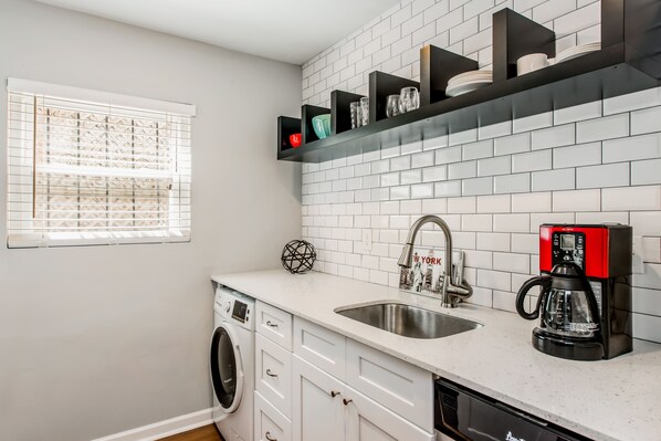 A modern kitchen with a built-in dishwasher, a coffee maker, and a window with blinds.