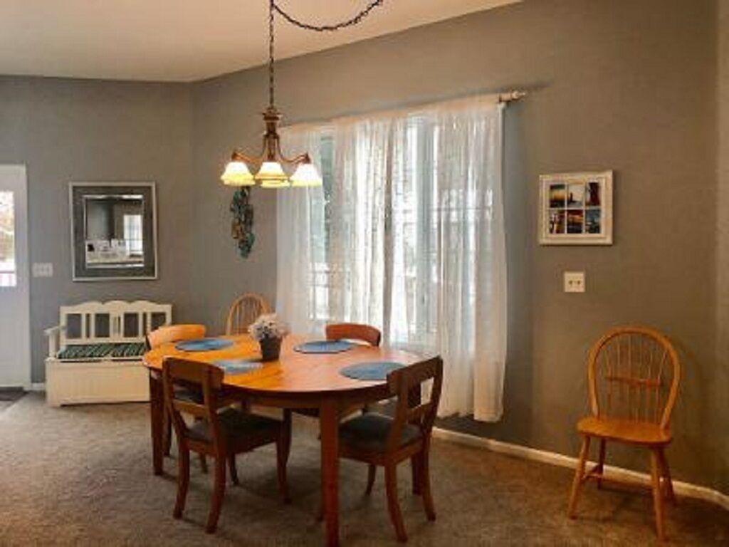 Comedor con mesa de madera, cuatro sillas, una lámpara de araña, un banco y una ventana con cortinas.