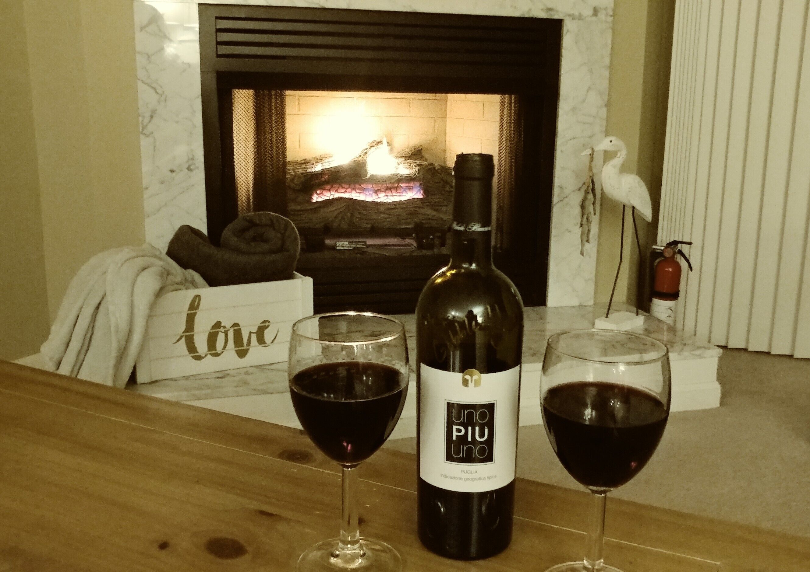 A bottle of wine and two glasses on a table in front of a fireplace.