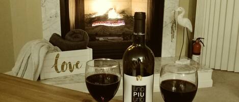 A bottle of wine and two glasses on a table in front of a fireplace.