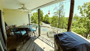 A covered porch with a table and chairs, a ceiling fan, and a view of trees and a distant building.