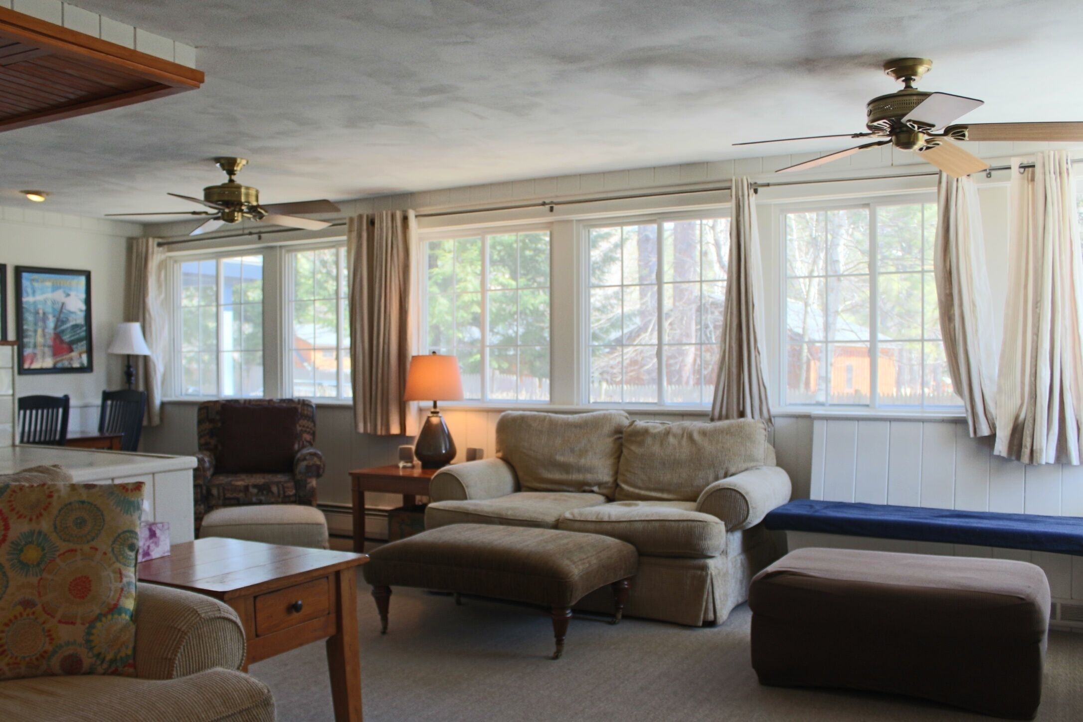 A living room with a sofa, ottoman, and armchair, a coffee table, a lamp, and a ceiling fan.