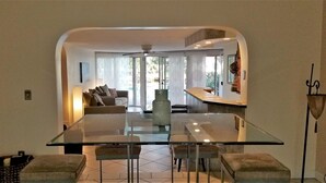 Uma sala de estar moderna com uma mesa de jantar de vidro, cadeiras estofadas, um sofá e uma mesa de centro.