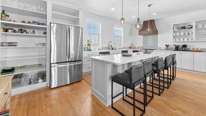 A modern kitchen with a central island, bar stools, and built-in shelving. - Sol Mate-Elevator,Beach,Firepit rooftop,Arcade (St. Augustine)