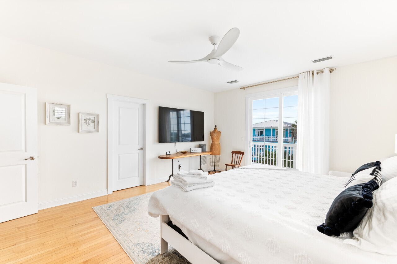 Une chambre avec un lit, un ventilateur de plafond, une télévision, un bureau et une vue sur l’extérieur.