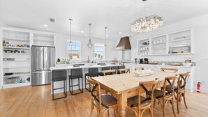 A modern kitchen with white cabinetry, a stainless steel refrigerator, a wooden dining table with six chairs, and pendant lighting. - Sol Mate-Elevator,Beach,Firepit rooftop,Arcade (St. Augustine)