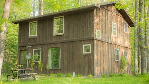 A rustic wooden cabin with multiple windows, surrounded by lush greenery and trees. - Rustic Two Level Tree Lodge Surrounded By The Forest With Fireplace And Fire Pit (McGrath)