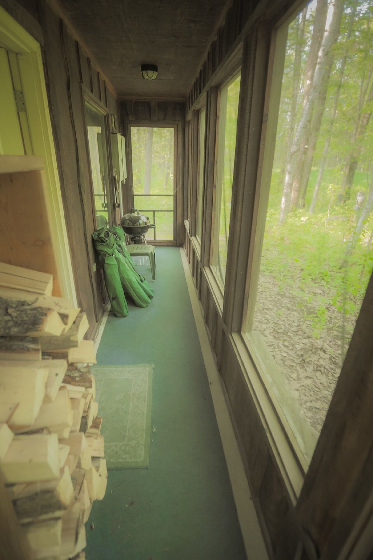 Un couloir étroit aux murs en bois et au sol vert, qui mène à une fenêtre donnant sur une forêt.