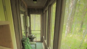 A narrow hallway with wooden walls and a green floor, leading to a window with a view of a forest. - Rustic Two Level Tree Lodge Surrounded By The Forest With Fireplace And Fire Pit (McGrath)