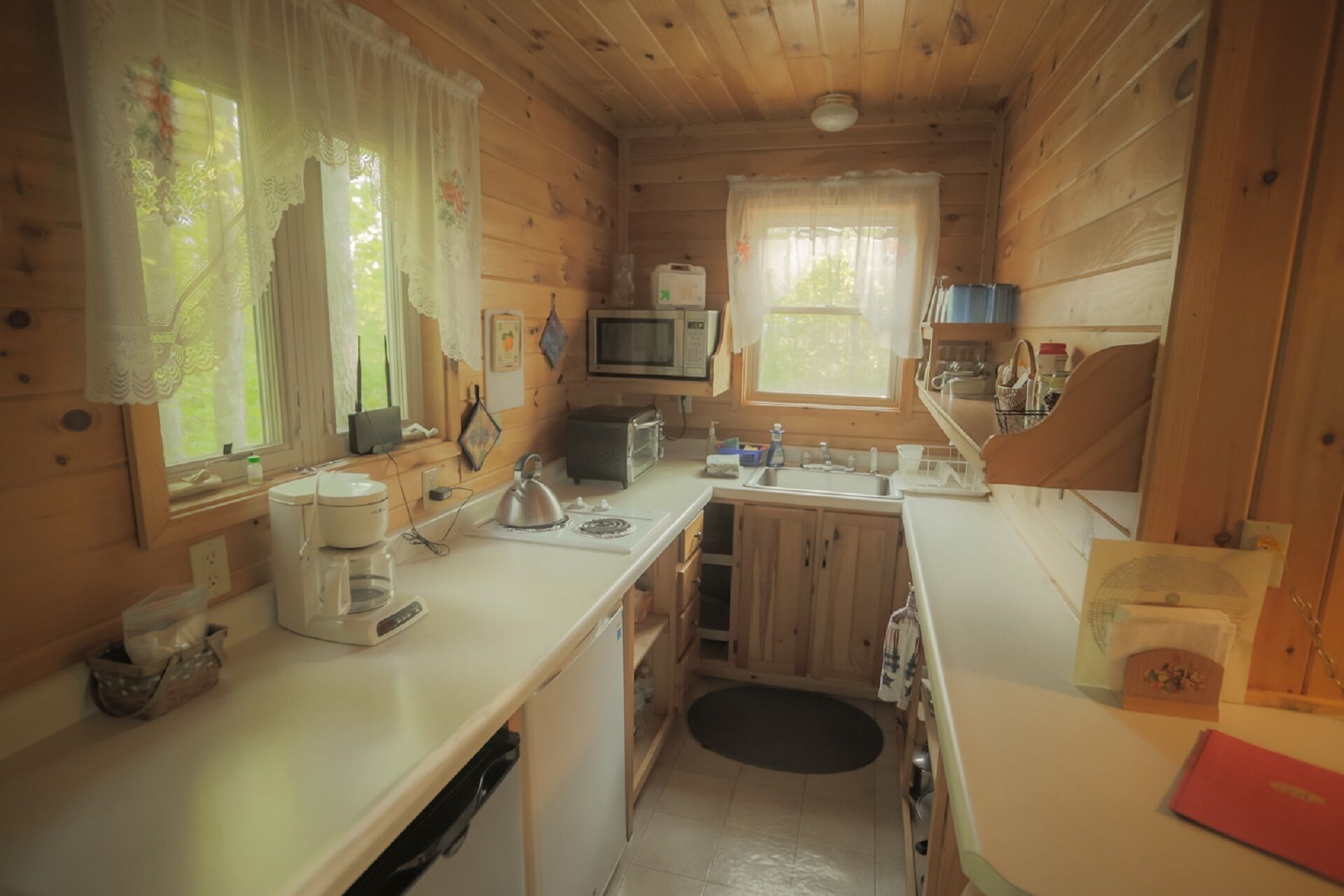 Een kleine keuken met houten wanden, een magnetron, waterkoker en een spoelbak.