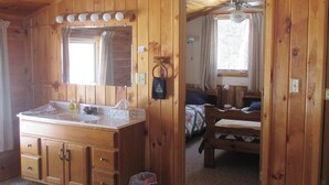 A wooden cabin interior with a large wooden vanity, a bed, and a small table. - Rustic Two Level Tree Lodge Surrounded By The Forest With Fireplace And Fire Pit (McGrath)