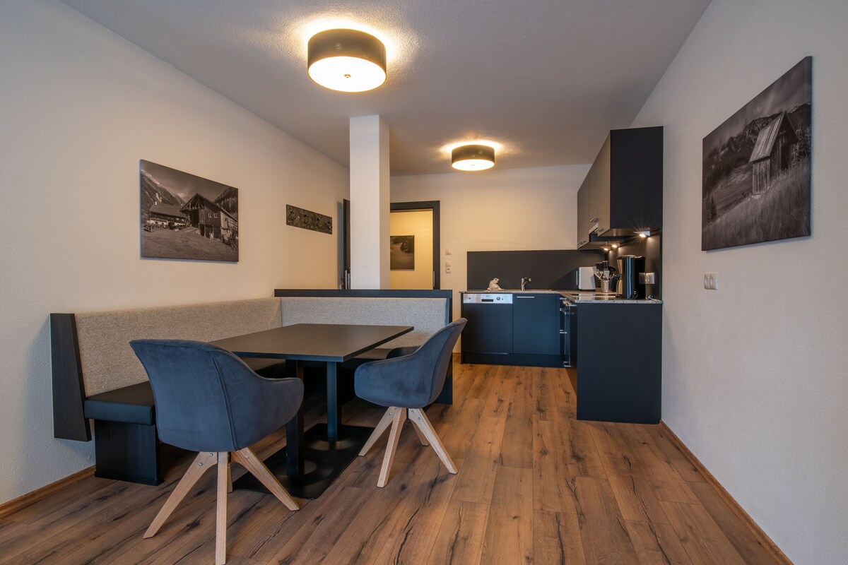 A compact kitchen with modern appliances, a dining area with a table and chairs, and artwork on the walls.