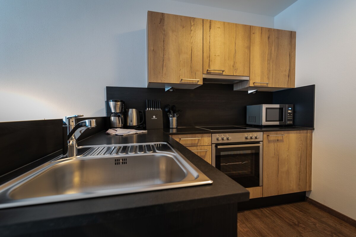A modern kitchen with wooden cabinets, stainless steel appliances, and a black countertop.