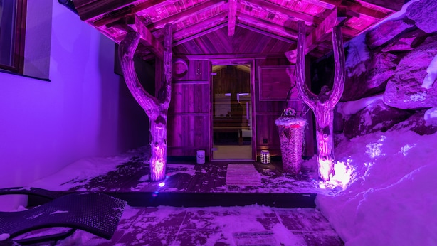 Una cabaña de madera con entrada cubierta de nieve e iluminación morada.