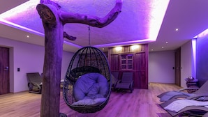 Una habitación con una hamaca colgante, suelo de madera e iluminación morada en el techo.