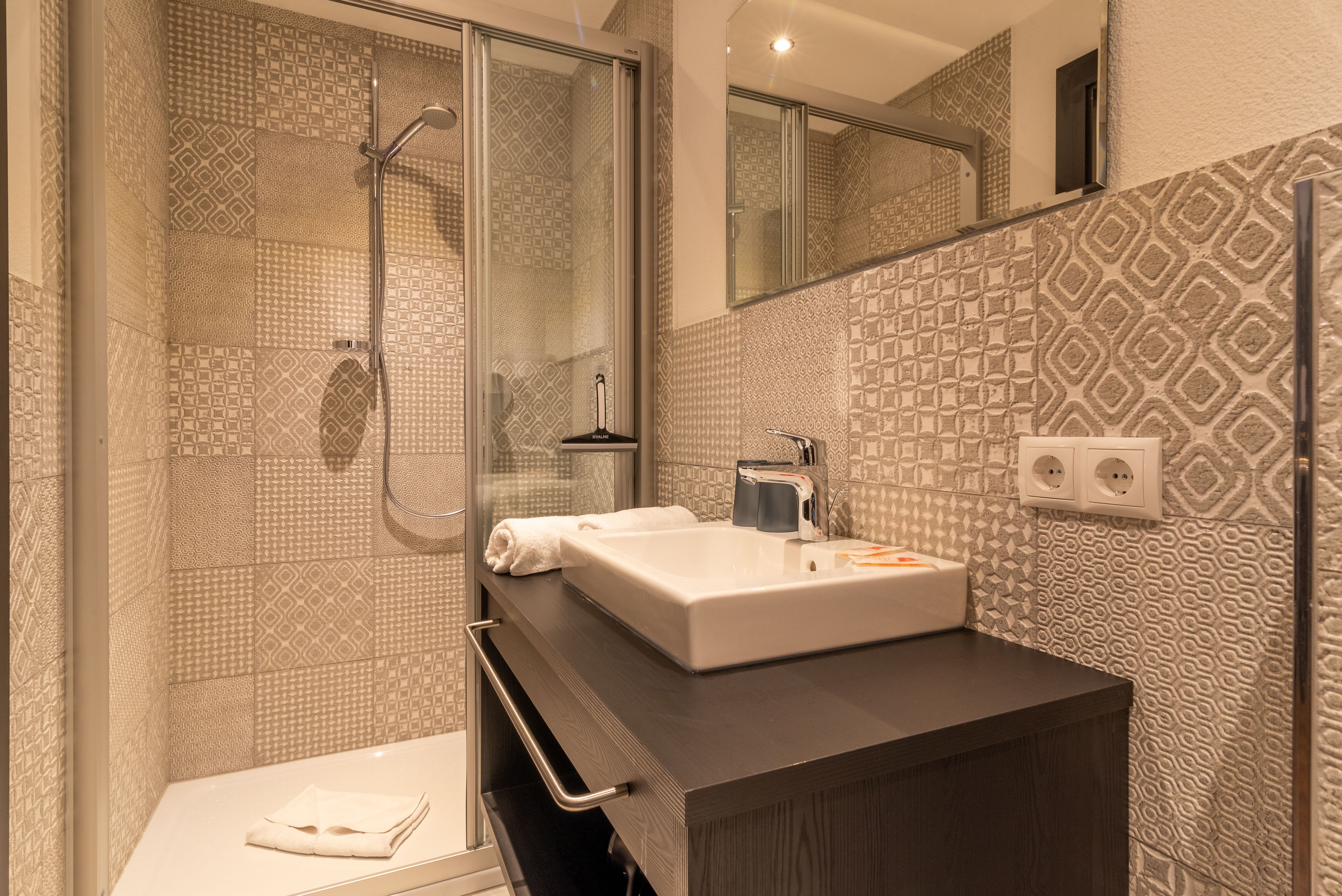 Ein modernes Badezimmer mit einer gläsernen Duschkabine, einem weißen Waschbecken und fliesenbesetztem Boden.