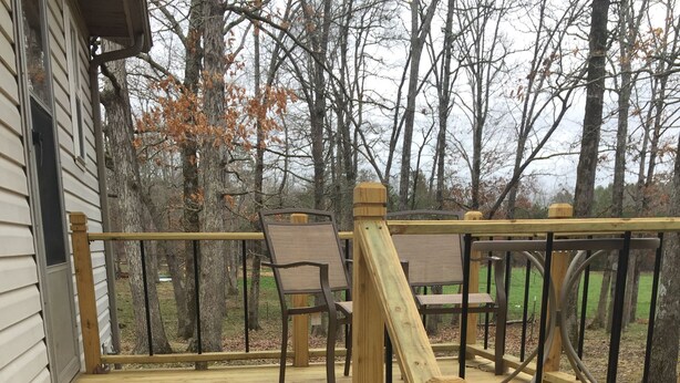 A wooden deck with steps leading to a house, surrounded by trees.