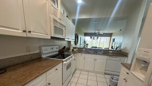 A kitchen with white cabinets, a microwave, stove, dishwasher, granite countertop, and a ceiling fan. - Wonderful, spacious 3 bedroom, 2 bath unit, enjoy free Golfing this Summer (Naples)