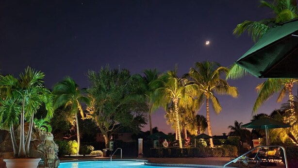 A nighttime pool area with palm trees, a pool, and a covered seating area. - Wonderful, spacious 3 bedroom, 2 bath unit, enjoy free Golfing this Summer (Naples)