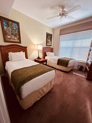 Une chambre d’hôtel avec deux lits, un ventilateur de plafond, une fenêtre avec des stores et des œuvres d’art accrochées aux murs.