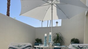 Un espace patio avec des chaises et une table en métal blanc, un grand parasol et des plantes en pot.