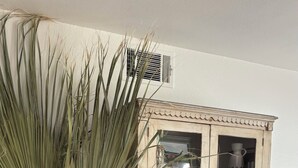 Une pièce avec une grande plante en pot, un meuble ancien aux portes vitrées et un sol carrelé.