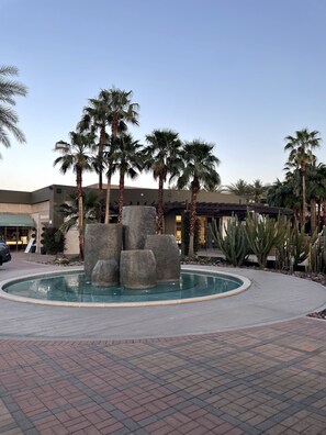A landscaped area with a circular pool, palm trees, and a building with a Tiffany & Co. sign.