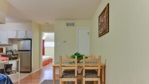 A compact kitchen with white cabinets, a stainless steel refrigerator, and a dining area with a wooden table and chairs.