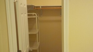 A narrow walk-through closet with white shelving units and a wooden rod.