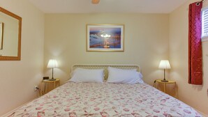 A bedroom with a bed, two bedside lamps, a ceiling fan, a framed picture on the wall, and a window with curtains.