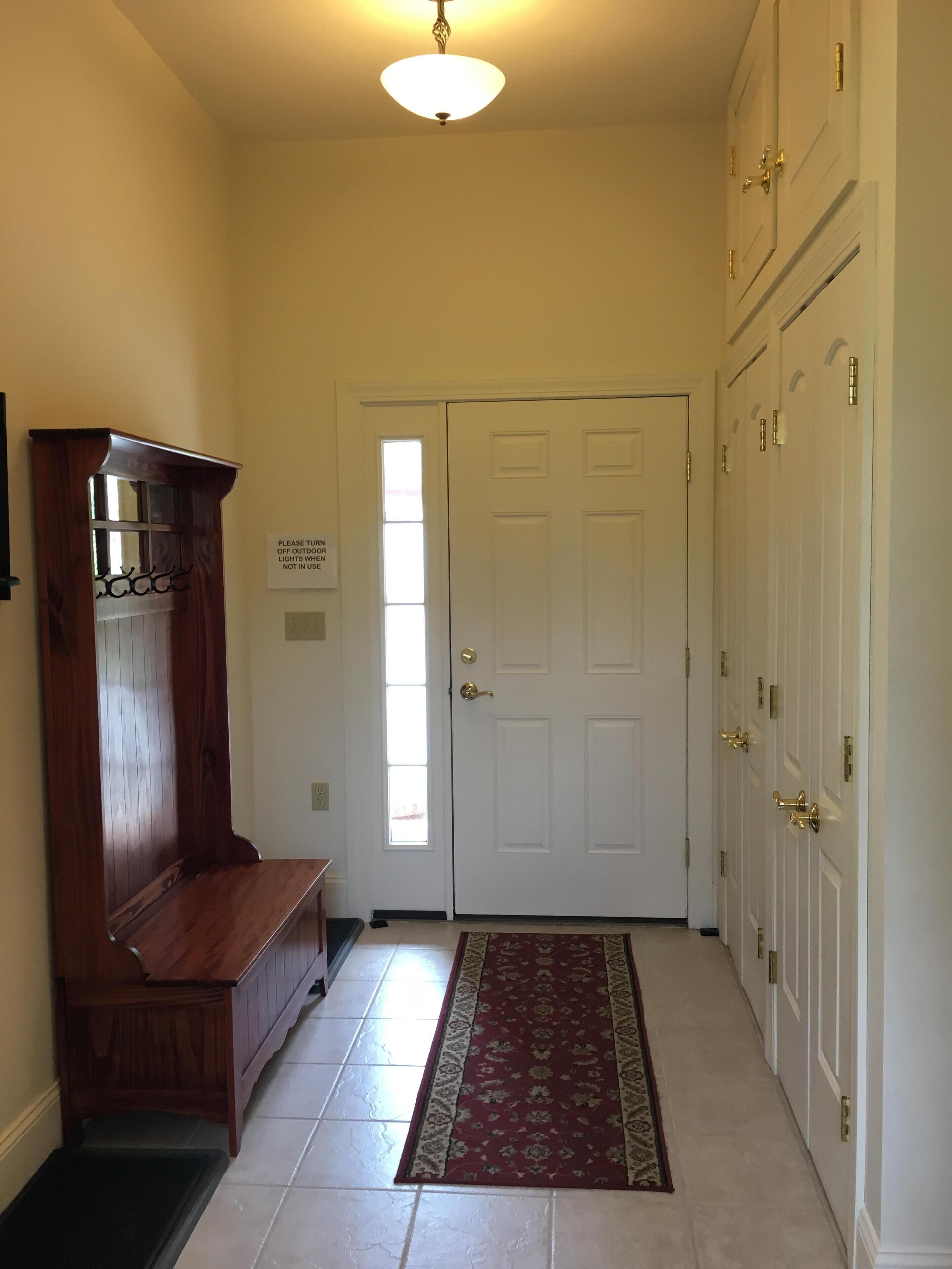 A hallway with a wooden bench, a rug, and a door with a sign.