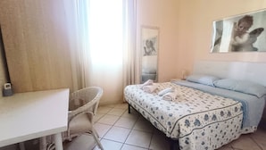 A hotel room with a bed, a chair, a desk, and a mirror.