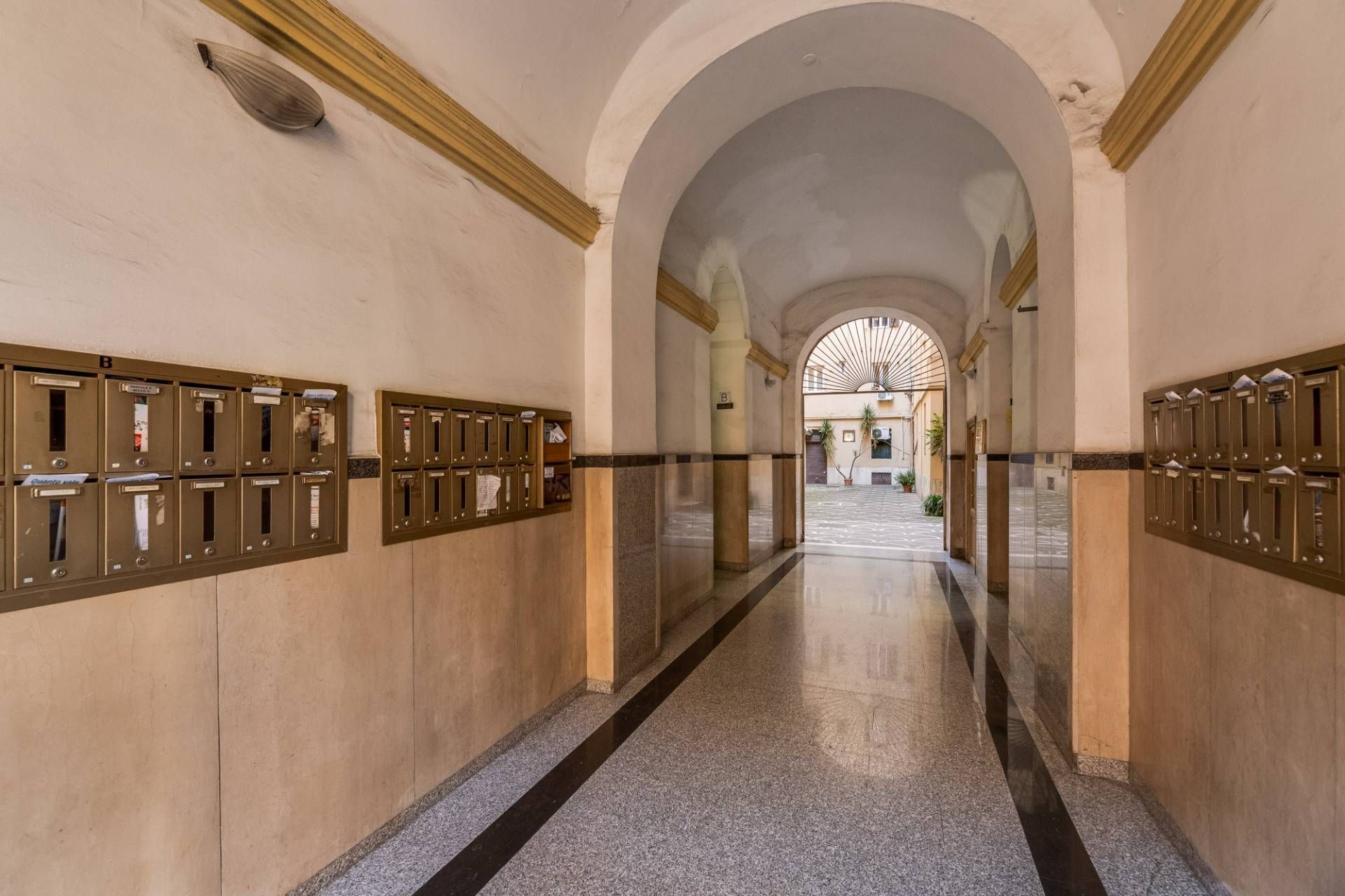 A hallway with mailboxes on both sides, leading to an arched doorway.