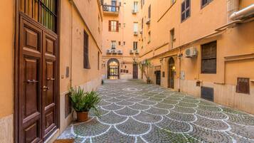 A narrow alleyway with patterned cobblestone pavement, wooden doors, and balconies with air conditioning units.