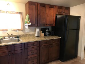 A kitchen with wooden cabinets, a granite countertop, a black refrigerator, a coffee maker, and a sink with a faucet. - Luxury 1 Bedroom casita in historic house in central Tucson (Tucson)