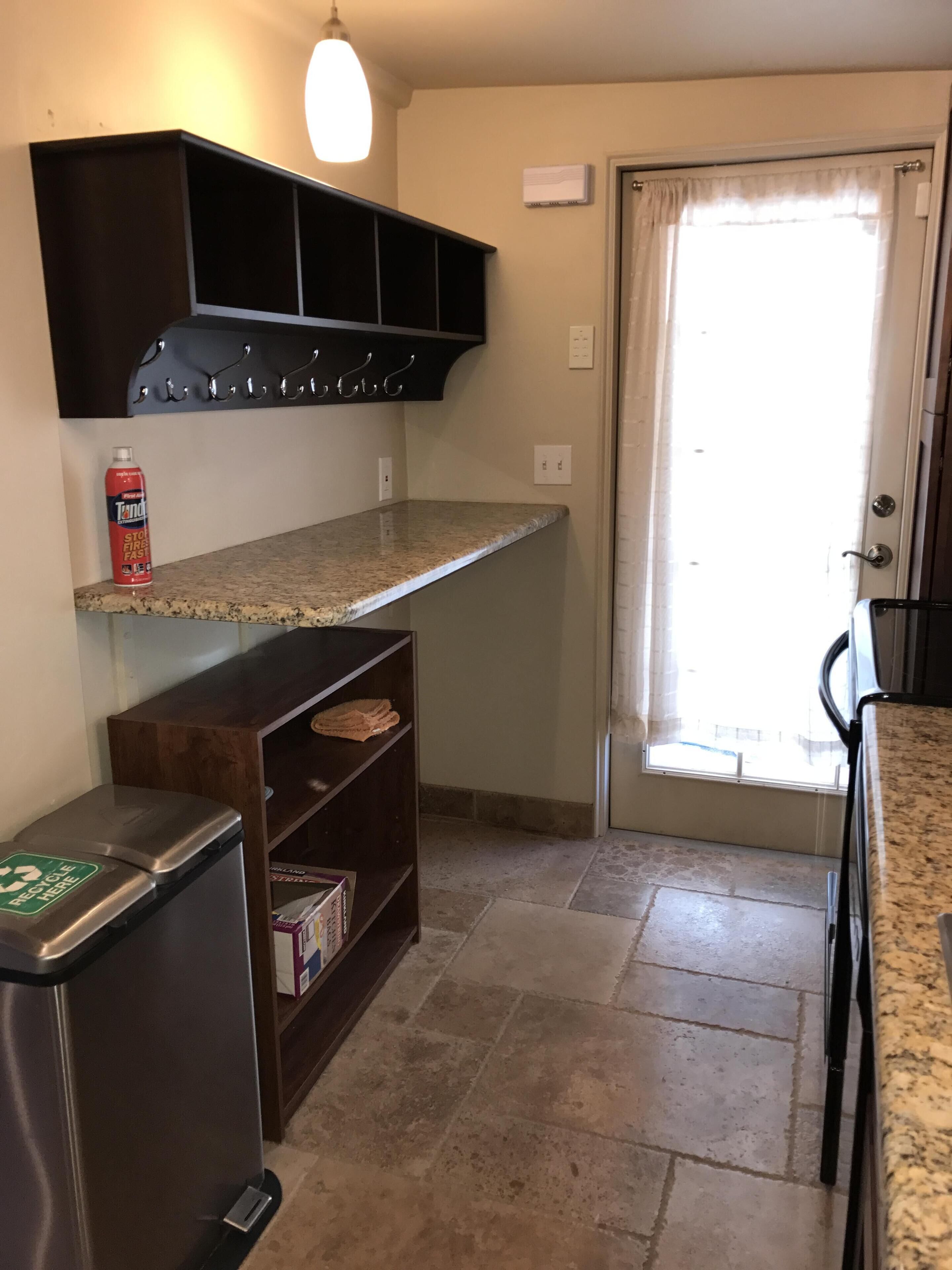 A kitchen with a granite countertop, a built-in oven, a refrigerator, and a window with a curtain.