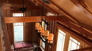 A cabin interior with a loft bed, a ceiling fan, and a hanging light fixture.