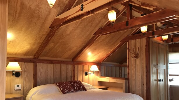 A wooden bedroom with a large bed, two bedside lamps, and a wooden wardrobe.