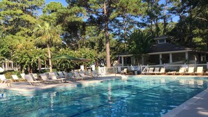 A swimming pool with lounge chairs and umbrellas, surrounded by trees and a building with a covered patio. - NEWLY RENOVATED, Nicely Equipped, Steps to the Beach, Perfect for Families (Hilton Head Island)
