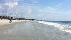A beach with a sandy shore, a few people, and umbrellas. - NEWLY RENOVATED, Nicely Equipped, Steps to the Beach, Perfect for Families (Hilton Head Island)