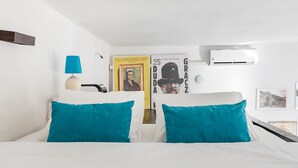 A hotel room with a bed, a lamp, an air conditioner, and a poster on the wall.
