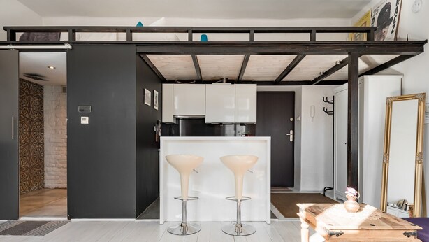 A modern kitchen with white cabinets, two bar stools, and a wooden table with a vase.