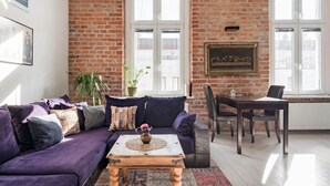 A living room with a brick wall, a purple sofa, a wooden coffee table, and a dining table with chairs.