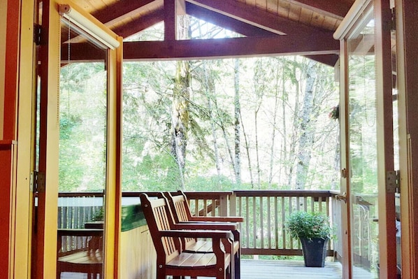 A covered porch with wooden chairs and a potted plant.