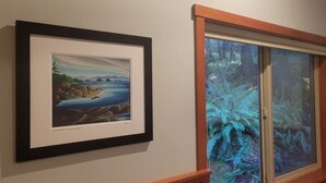 Un cuadro con paisaje enmarco y una ventana con vista a un bosque.