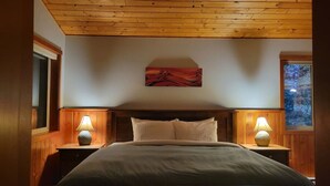 Un dormitorio con techo de madera, una cama con ropa de cama blanca, dos lámparas de noche y un cuadro en la pared.